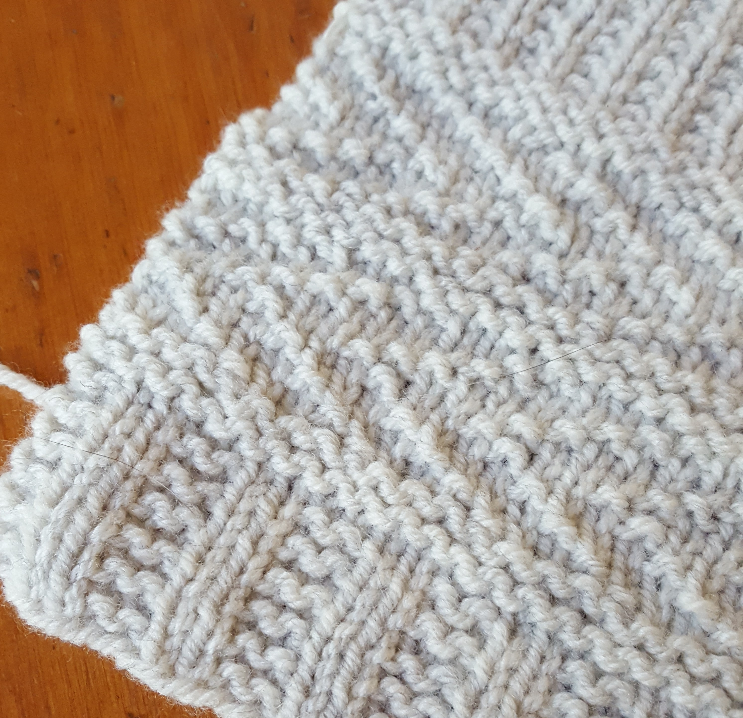 Photo shows a knitted swatch with a textured pattern in light gray yarn.