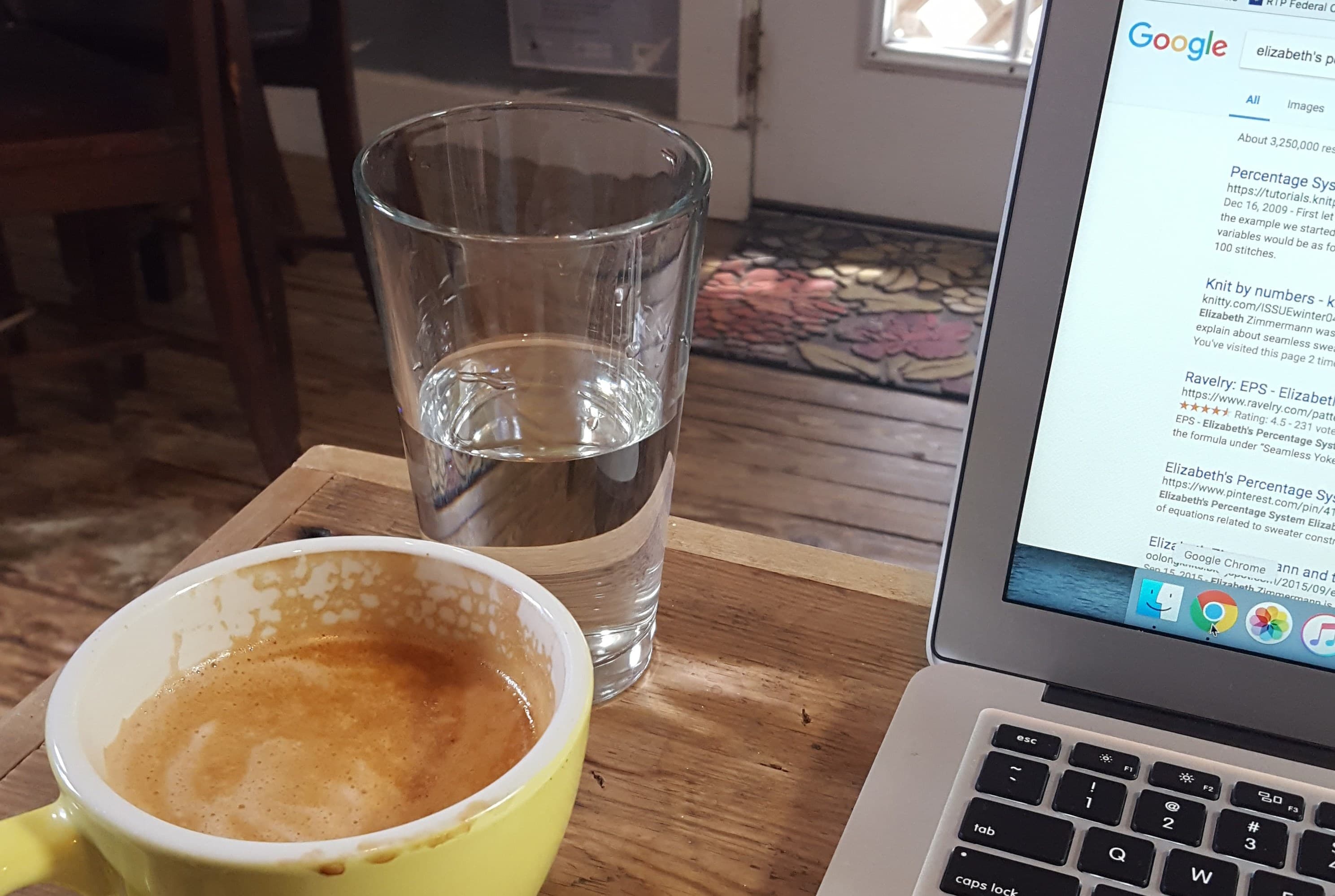 A laptop sits open on a wood table next to a glass of water and a cup of coffee.